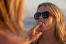 TETON_TORTOISE_GREY Man putting gum in woman's mouth wearing Ombraz teton armless sunglasses with strap