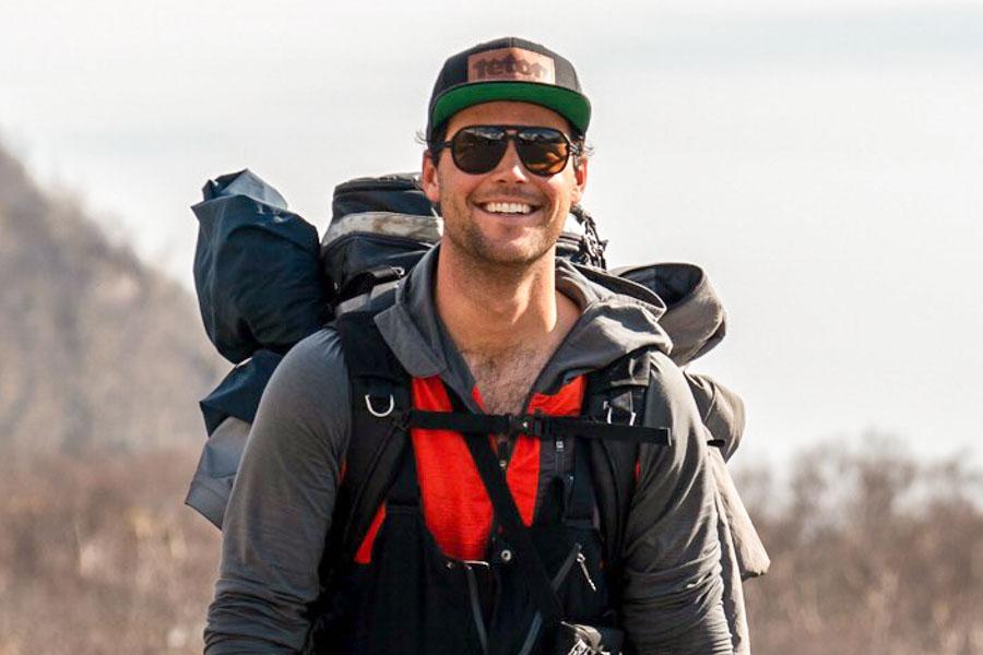 charcoal_brown Man carrying a hiking backpack smiling wearing Ombraz armless string sunglasses