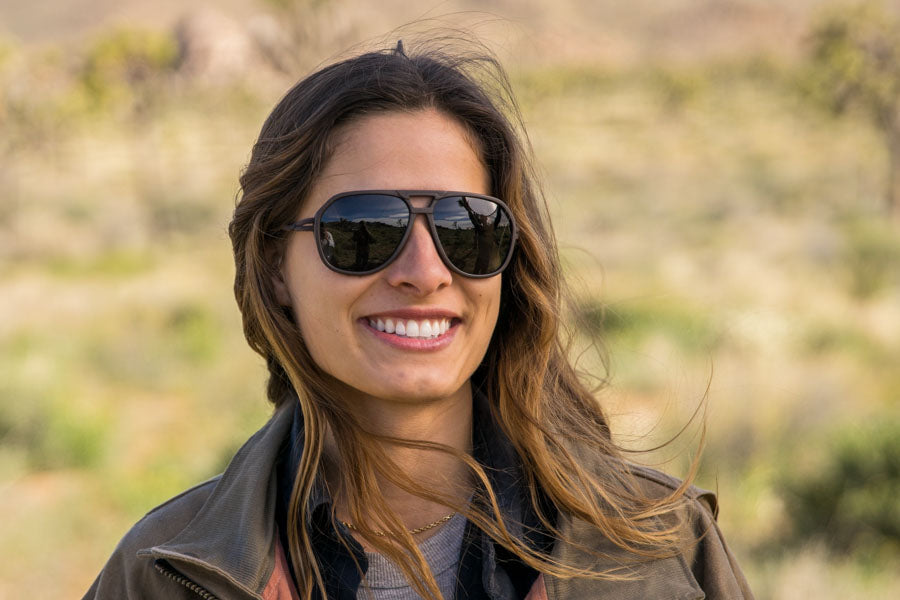 MATTEBROWN_GREY Woman smiling in nature wearing a pair of Ombraz classic armless sunglasses with cord