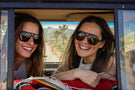 MATTEBROWN_BROWN Two women in the back of a car smiling wearing Ombraz classic armless string sunglasses