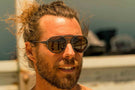 dolomite_charcoal_brown Bearded surfer at the beach wearing Ombraz armless strap sunglasses