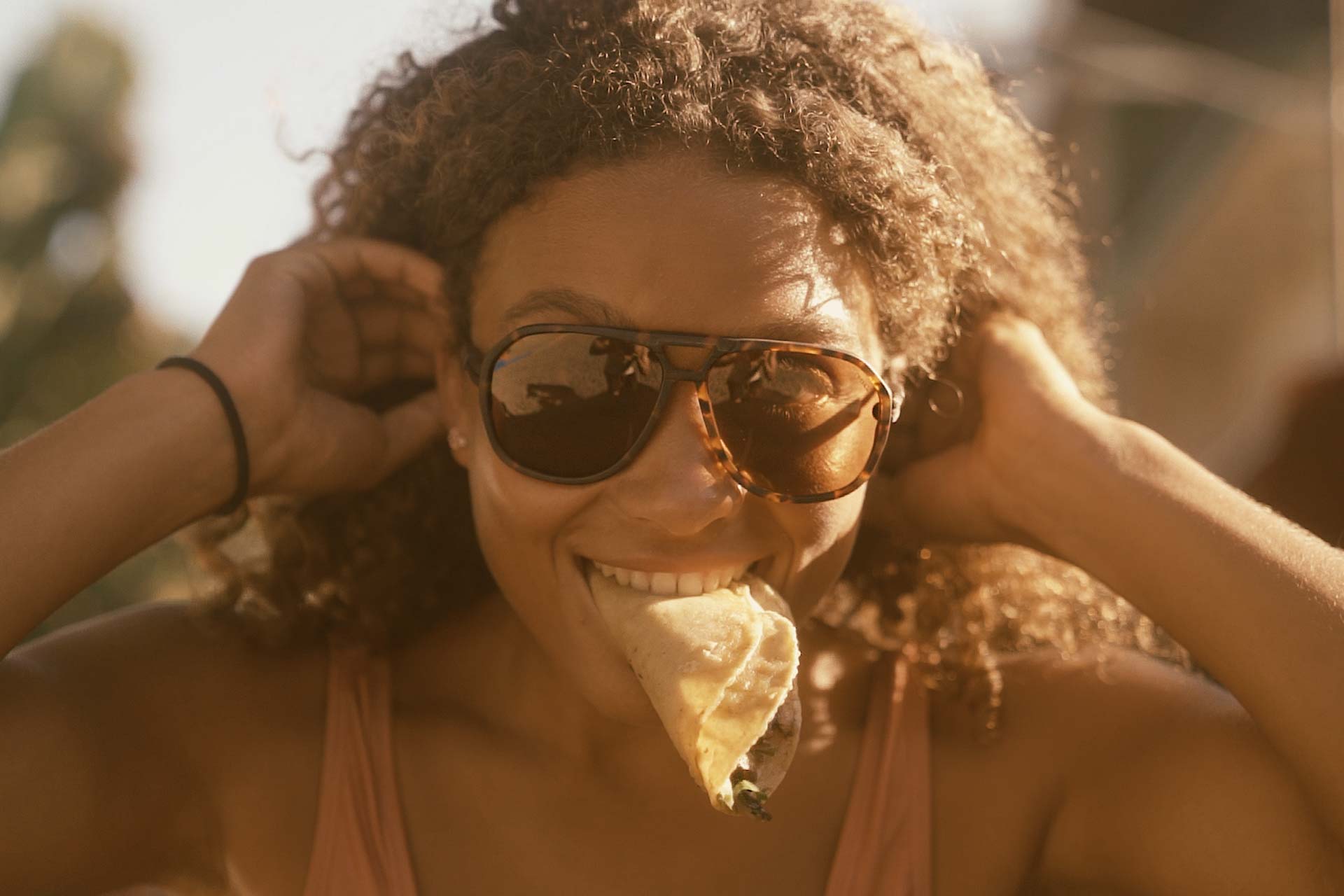 Tortoise_brown Woman eating tacos wearing ombraz classic armless sunglasses with strap