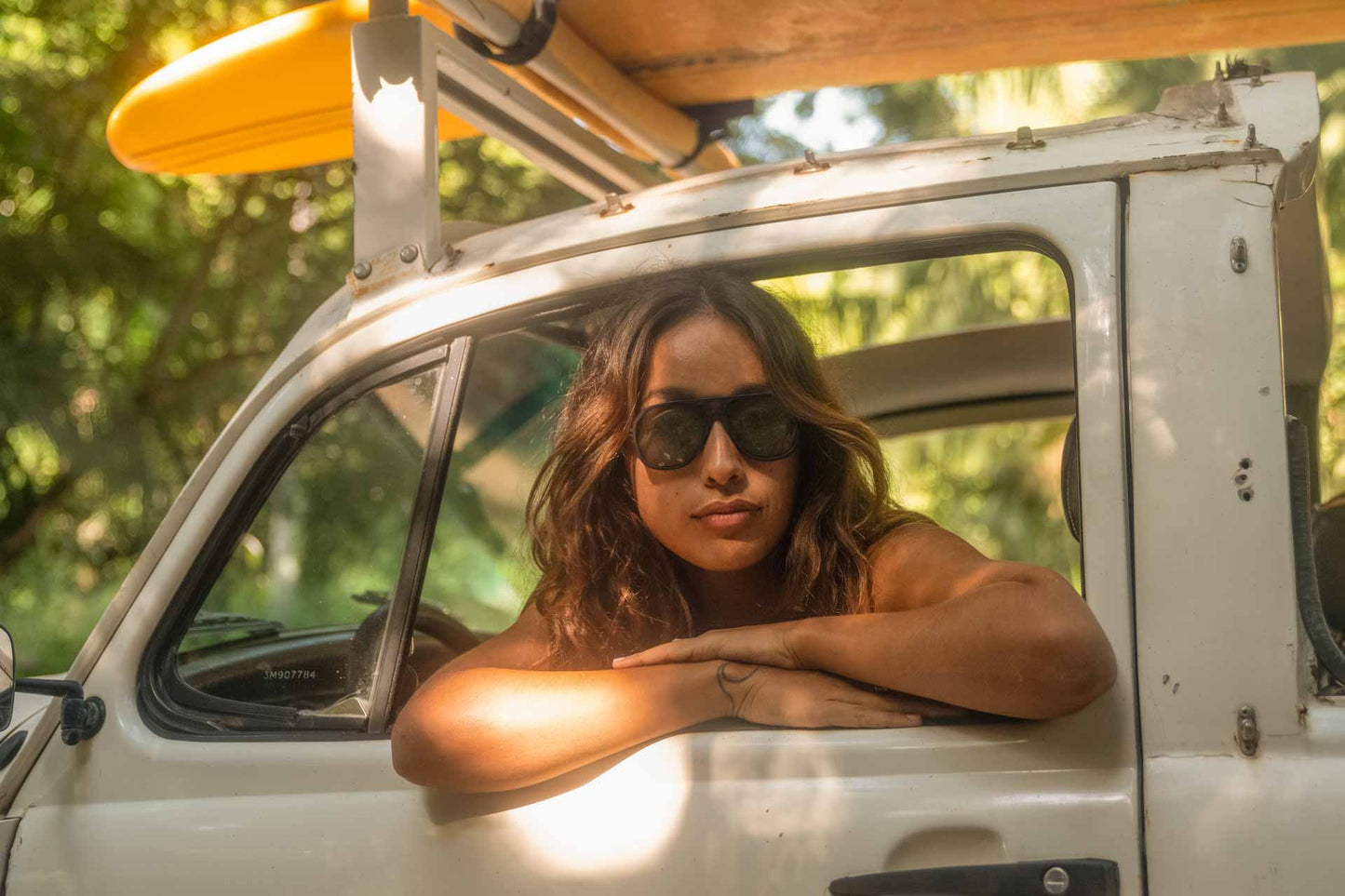 charcoal_brown Woman posing in her car carrying surfboards wearing Ombraz classic armless strap sunglasses 