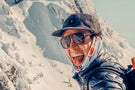 charcoal_grey Man with tongue out in the snowy mountains wearing Ombraz classic armless strap sunglasses