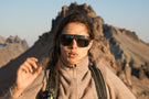 Woman in front of a mountain range wearing Ombraz unisex classic armless strap sunglasses with side shields