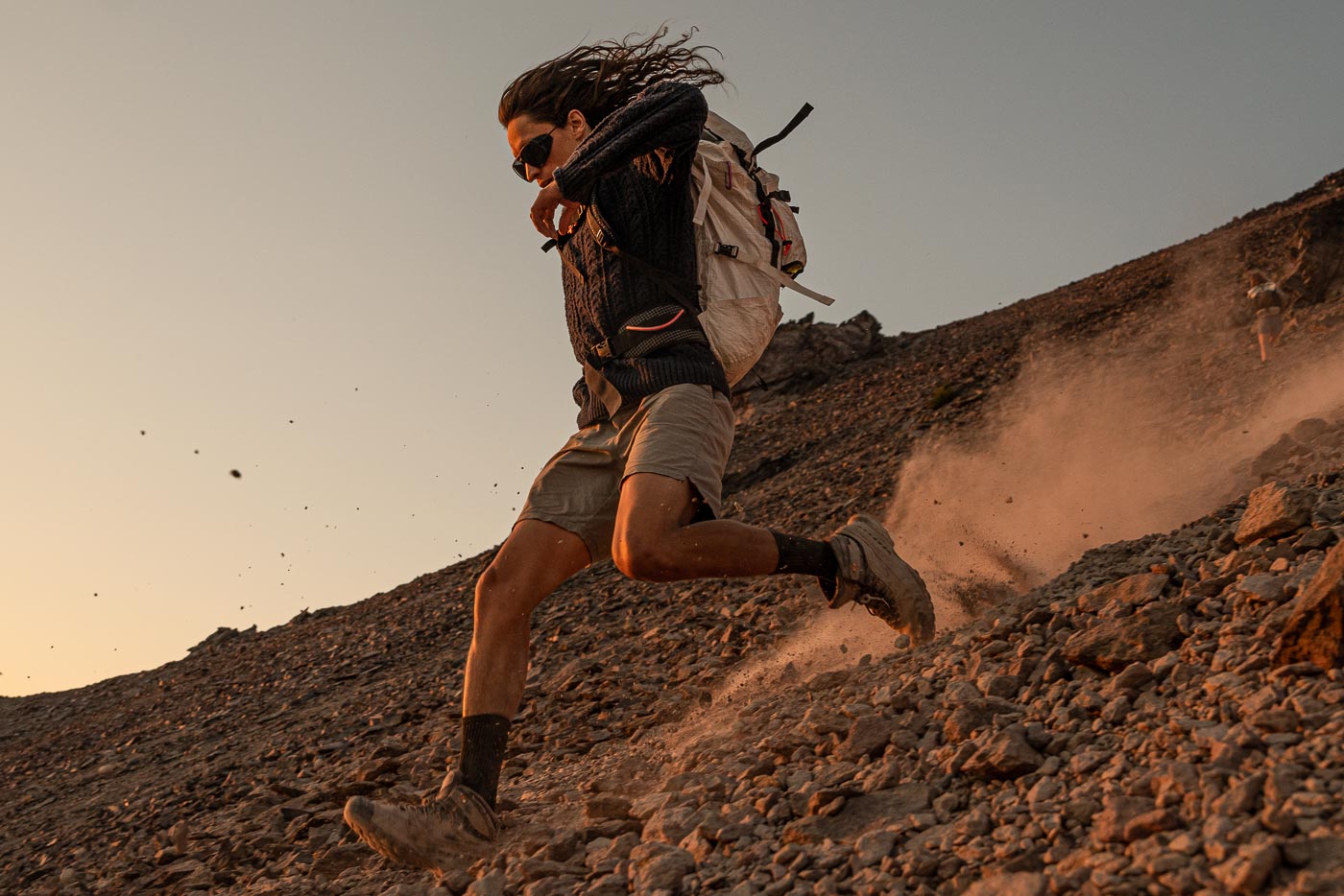 Man running down a rocky slope wearing Ombraz classic unisex armless string sunglasses with side shields
