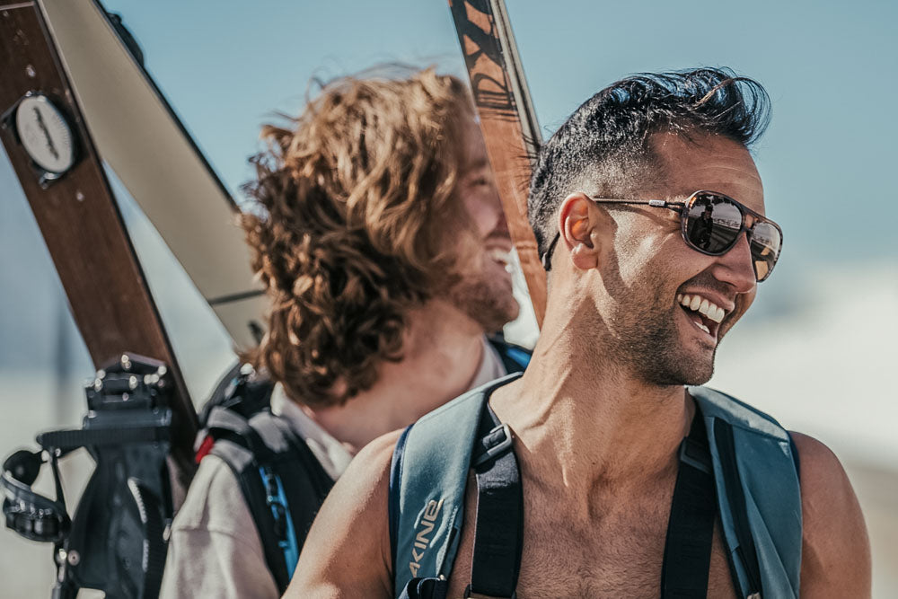 ember_brown Two smiling guys with skis wearing Ombraz leggero armless sunglasses with strap
