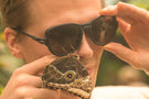 Close up of man wearing Ombraz armless rope sunglasses with a butterfly hanging from them TETON_CHARCOAL_yellow