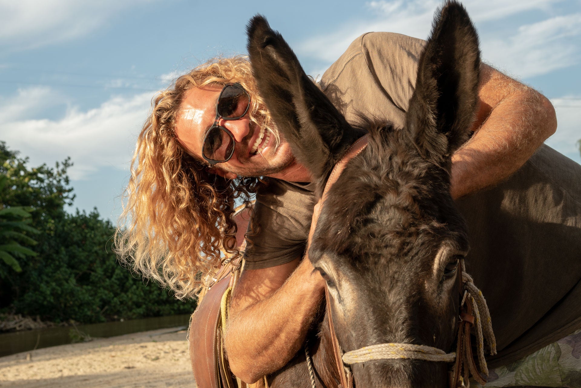 Man smiling next to a donkey wearing Ombraz teton armless sunglasses TETON_TORTOISE_YELLOW