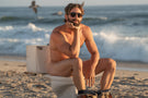 Man sitting on a toilet on a beach naked wearing Ombraz viale armless string sunglasses VIALE_CHARCOAL_BROWN
