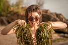 Portrait of a woman holding seaweed with her tongue out wearing Ombraz viale armless rope sunglasses VIALE_CHARCOAL_BROWN