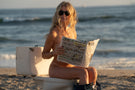 VIALE_CHARCOAL_GREY Naked woman on the beach reading a newspaper wearing Ombraz armless sunglasses with strap