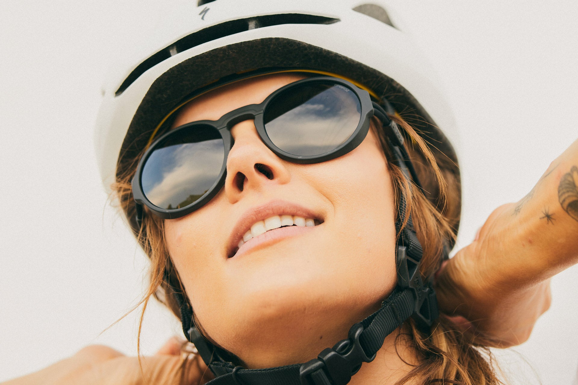 VIALE_CHARCOAL_GREY Close up of woman in a helmet looking up wearing Ombraz viale unisex armless string sunglasses