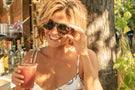VIALE_DUSK_BROWN Woman holding a drink smiling wearing Ombraz viale armless sunglasses with cord